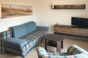 Ein Wohnzimmer mit einer Couch, einem Couchtisch, einem Fernseher und einem Bücherregal.
