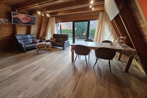A cozy loft-style room with a wooden ceiling, a dining table with chairs, a sofa, and a large window with curtains. - Dream in Carolinensiel (Carolinensiel)