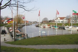 Blick auf einen Fluss mit vertäuten Booten, Flaggen und Gebäuden am Ufer.