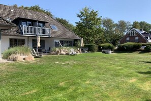 A two-story house with a balcony, a lawn, and a neighboring house. - Langeneß in the house Achter de Dünen (Sankt Peter-Ording)