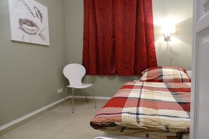 Een slaapkamer met een bed, een stoel, een rood gordijn en een wandlamp.