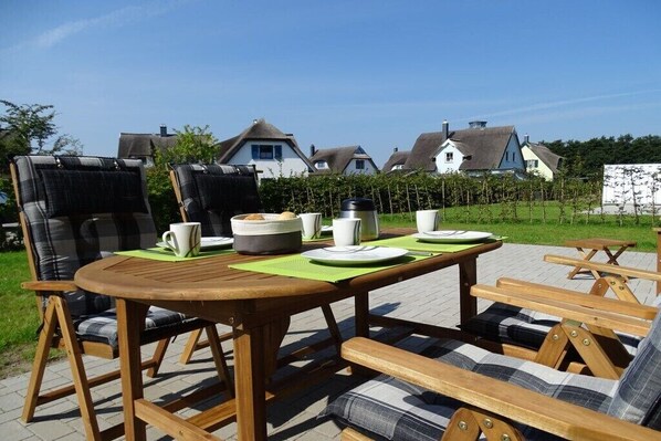 Een terras met een houten tafel en stoelen, omringd door huizen.
