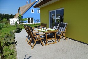 Un patio con tavolo e sedie, una casa blu sullo sfondo e un muro verde.