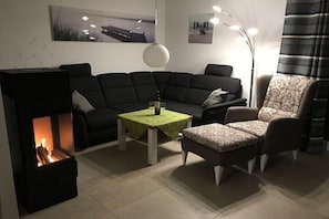 Een woonkamer met een bank, fauteuil, tafel en open haard.