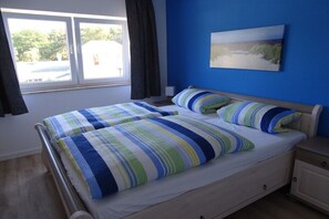 Un letto matrimoniale con lenzuola a righe, un comodino, una lampada da tavolo, una finestra con tende e un quadro appeso al muro.