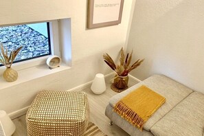 Ett vardagsrum med en soffa, ett litet runt bord, en dekorativ vas och ett fönster med utsikt över småstenar.