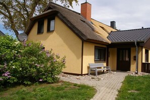 Ein gelbes Haus mit einem Strohdach, einem Schornstein und einer Bank davor.