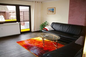 Ein Wohnzimmer mit einer schwarzen Ledersofa, einem Glastisch und einem farbenfrohen Teppich.