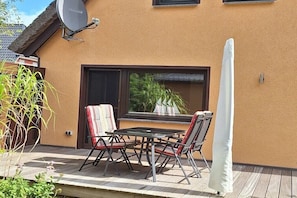 Eine Terrasse mit Tisch und Stühlen, einer Satellitenschüssel und einem Fenster mit Blick auf Grünflächen.
