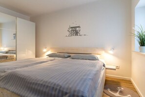 Ein Schlafzimmer mit einem Bett, Nachttischen, einem an der Wand befestigten Kunstwerk und einer Topfpflanze.