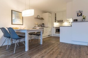 Eine moderne Küche mit weißen Schränken, einem Essbereich mit Tisch und Stühlen sowie einer hängenden Leuchte.