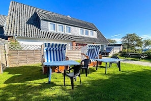 Ein Haus mit Ziegeldach, einem umzäunten Garten und Außenbereich mit gestreifter Markise.