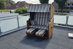 Ein Holzhocker mit gestreifter Polsterung auf einem Balkon mit Geländer.