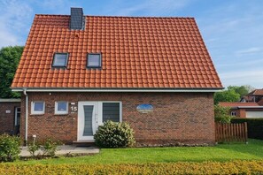 Ein zweistöckiges Backsteingebäude mit rotem Ziegeldach und einer kleinen Veranda, mit einem Schild, das den Namen 'Haus Karin' anzeigt.