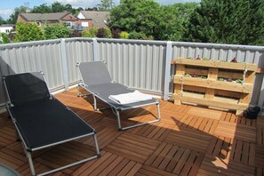 Eine Dachterrasse mit zwei Liegestühlen, einem Pflanzkasten aus Holz mit Pflanzen und einem Metallgeländer.