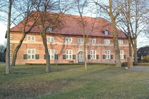 Ein großes Backsteinhaus mit rotem Ziegeldach, zahlreichen Fenstern und einem zentralen Eingang.