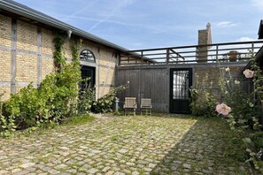 Ein Innenhof mit einem Backsteinhaus, zwei Holzstühlen und einem Metallgeländer.