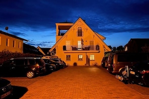 Ein zweigeschossiges Gebäude mit Balkon, parkenden Autos und befestigter Auffahrt.