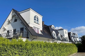 Ein großes, weißes mehrgeschossiges Haus mit einem steilen Walmdach, mehreren Schornsteinen und einem Balkon mit schwarzem Geländer.