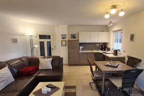 Ein kompakter Wohnbereich mit Sofa, Esstisch, Stühlen, einer Küchenzeile und einer Tür zu einem weiteren Raum.