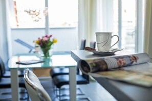 En matplats med ett bord, stolar, en kopp, en tallrik och en hoprullad tidning.