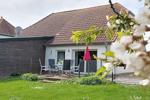 Ein Haus mit einem Ziegeldach, einem umzäunten Garten und einer Terrasse mit Stühlen und einem Tisch.