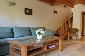 Ein Wohnzimmer mit Couchtisch aus Holz, einem grünen Sofa, einem Korbstuhl und einer Treppe.
