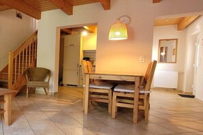 Ein Essbereich mit einem Holztisch und Stühlen, ein Korbstuhl, eine Treppe und eine Küche im Hintergrund.