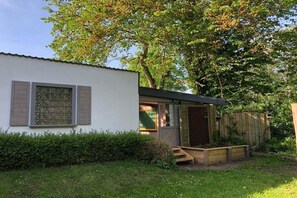 A small, single-story building with a white exterior and wooden shutters, a covered porch, and a wooden fence. - Holiday home with 3 bedrooms (Stelle- Wittenwurth)