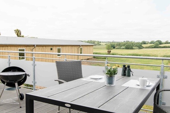A wooden deck with a table, chairs, a grill, binoculars, and a potted plant. - Willi's view of the meadow (Grödersby)