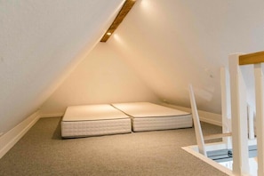 A small, sloped ceiling room with two white mattresses and a white railing. - Willi's view of the meadow (Grödersby)