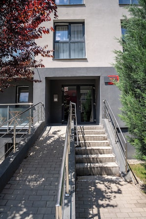 A building entrance with a staircase, a glass door, and a metal railing.