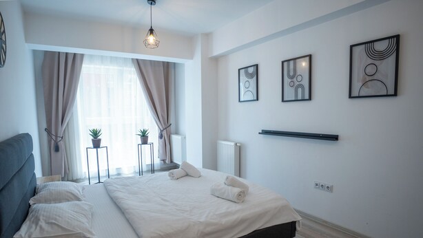 Un dormitorio moderno con cama, mesitas de noche y una ventana con cortinas.