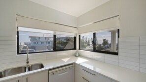 Eine moderne Küche mit integriertem Geschirrspüler, einer Edelstahlspüle und einem Fenster mit Blick auf eine Wohngegend.