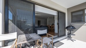Un patio con una mesa y sillas, y un amplio ventanal corredera que da a un espacio interior con sofá y mesa de comedor.