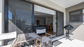 Eine Terrasse mit Tisch und Stühlen, eine Glastür, die zu einem Innenraum mit Sofa und Esstisch führt.