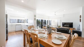 A modern kitchen with white cabinets and a dining area with wooden furniture. - Talinga 4 - Lifestyle Yamba (YAMBA)