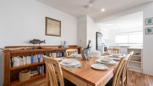 Un comedor con una mesa de madera dispuesta para cuatro personas, rodeado de estanterías, una escultura de pez y un mapa enmarcado en la pared.