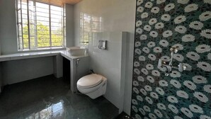 A bathroom with a toilet, sink, and shower. There is a window providing natural light. - The Riverside Estate (Udaipur)