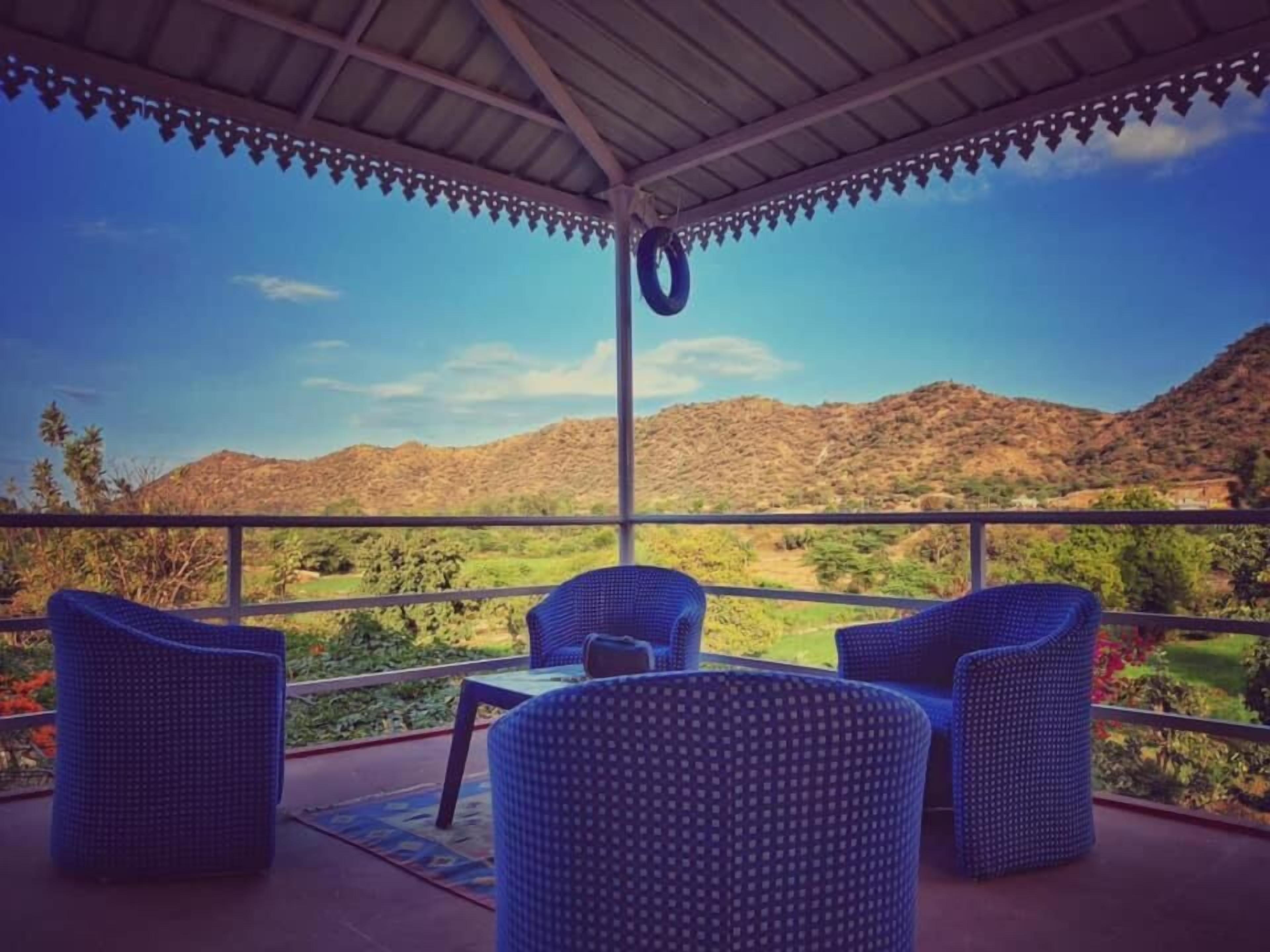 A covered outdoor seating area with wicker furniture and a view of a mountainous landscape.