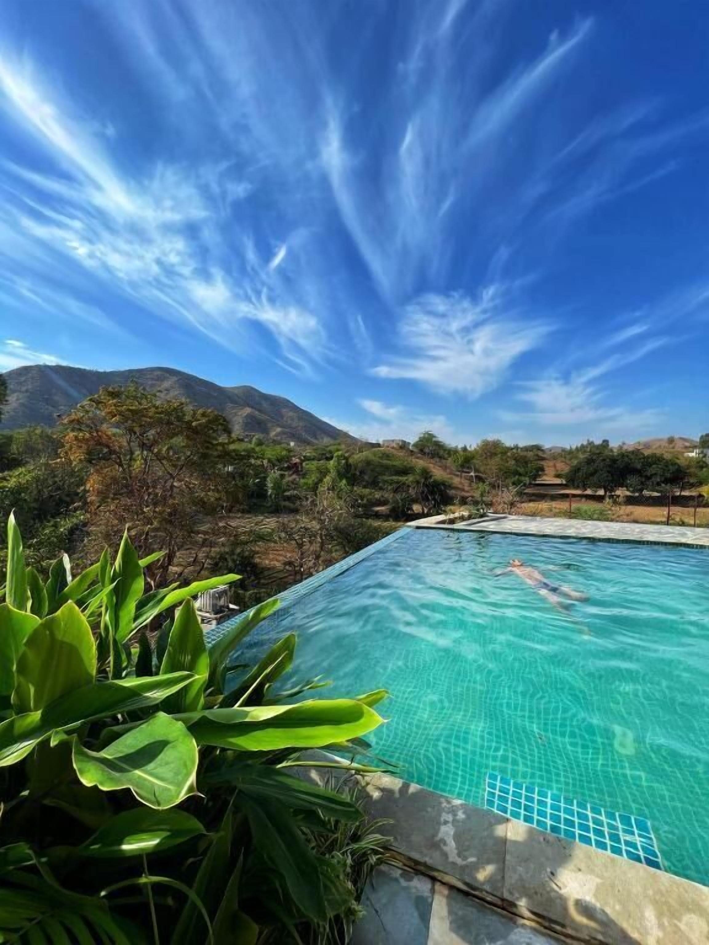A swimming pool with clear blue water, surrounded by greenery and mountains in the background.