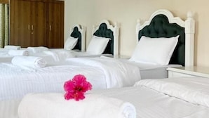A hotel room with two beds, a wooden wardrobe, and a single bed with a pink flower. - The Riverside Estate (Udaipur)