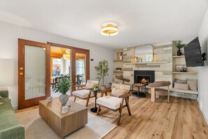 Sala de estar con chimenea, piso de madera y un comedor visible a través de un vidrio.