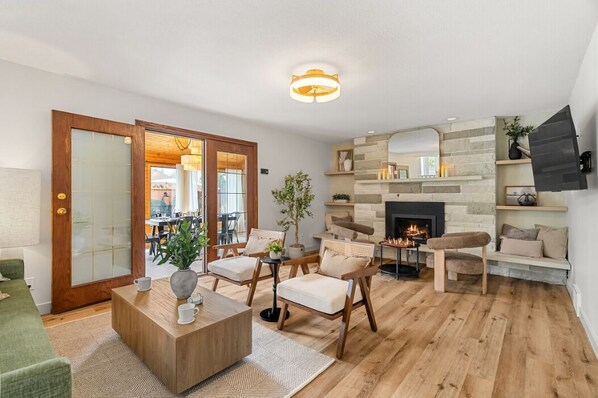 Sala de estar con chimenea, piso de madera y un comedor visible a través de un vidrio.