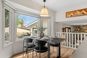 Un comedor de concepto abierto con una mesa dispuesta para cuatro, una lámpara colgante y vistas al exterior.