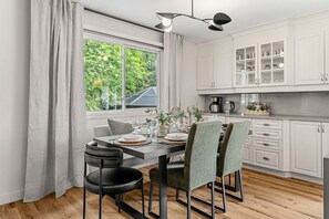 Eine moderne Küche mit weißen Schränken, einem Esstisch für vier Personen und einem großen Fenster mit Vorhängen.