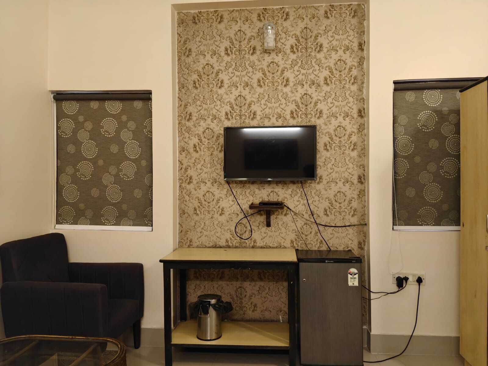 Une chambre avec un téléviseur fixé au mur, une petite table avec une bouilloire et une chaise.