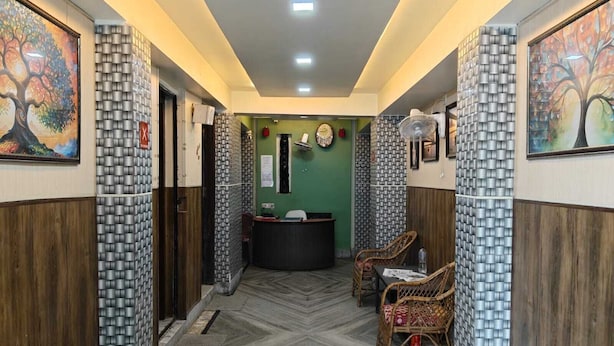 A hallway with patterned walls, a reception desk, and two wicker chairs. - Amit Hotel (Kolkata)