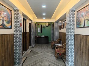 A hallway with patterned walls, a reception desk, and two wicker chairs. - Amit Hotel (Kolkata)