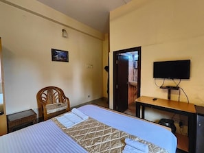 A bedroom with a bed, a chair, a desk, a television, and a door leading to another room.